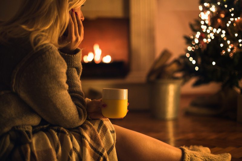 Woman sitting by the fireplace and drinking tea on Christmas Eve.